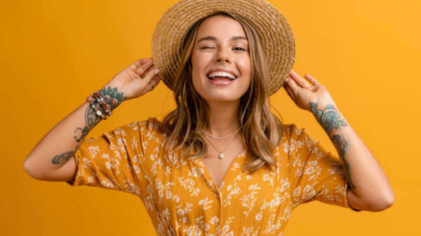 Mulher elegante em vestido amarelo e chapéu de palha posando em fundo amarelo, isolada, com expressão sorridente no rosto, feliz, com dentes brancos. Tendência de estilo de moda de verão.