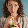 mulher bebendo suco verde em fundo azul