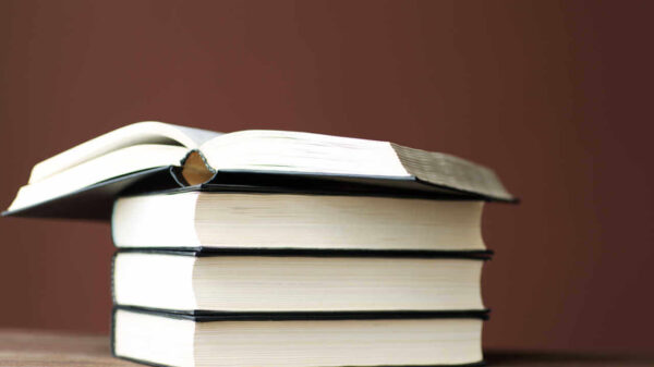 Quatro livros sobre uma mesa de madeira, empilhados. O do topo está aberto.