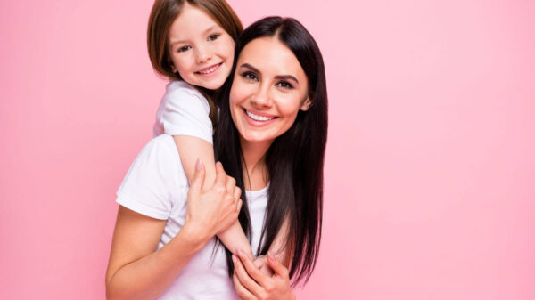 Foto de mulher jovem segurando/abraçando a filha. Isoladas em um fundo de cor rosa pastel.