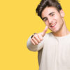Homem sorrindo, fazendo sinal positivo com os polegares, usando uma blusa branca de manga comprida, sobre fundo amarelo.