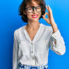 Jovem morena vestindo roupas casuais e usando óculos, sorrindo, fazendo sinal de "ok" com a mão e os dedos. Expressão de sucesso.