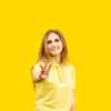 Jovem mostrando três dedos, vestida com uma camiseta amarela. Isolada no fundo amarelo.