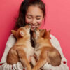 Mulher alegre recebendo beijinhos de dois filhotes de cachorro.
