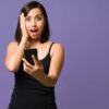 Mulher surpresa, olhando para a câmera enquanto usa seu smartphone.