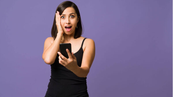 Mulher surpresa, olhando para a câmera enquanto usa seu smartphone.