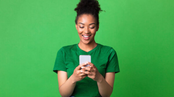 Retrato de mulher feliz, usando smartphone, contra uma parede verde de um estúdio.