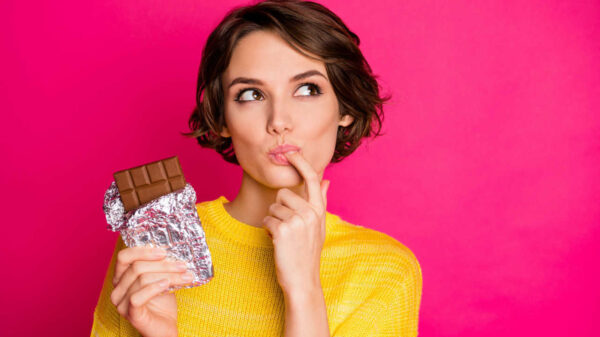 Retrato de mulher comendo chocolate, isolada sobre um fundo rosa.