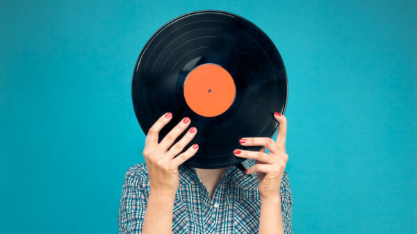 Imagem de mulher segurando disco de vinil na frente do rosto, no fundo azul.