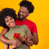 casal se abraçando com ela segurando uma rosa em fundo amarelo