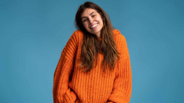 Retrato de uma jovem feliz, em pé, em uma parede azul, sorrindo sinceramente. Garota moderna sorrindo para a câmera, em pé, contra um fundo azul.