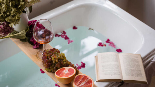banheira com taça de vinho, livro, frutas e pétalas