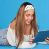 Menina mexendo no tablet, deitada no chão. Isolada no fundo azul.