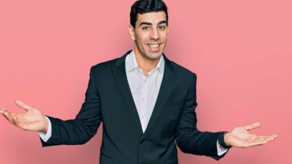 Homem vestindo roupas de negócios, sorrindo, mostrando as palmas das mãos abertas.