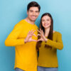 casal fazendo coração com as mãos em fundo azul