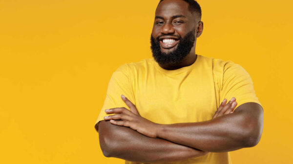 Jovem sorridente, alegre, satisfeito, positivo e feliz. Homem usando camiseta casual amarela, de braços cruzados, isolado em retrato de estúdio de fundo de cor amarela simples.