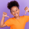 Foto de uma gratoinha jovem e alegre, feliz, sorrindo positivamente, apontando os polegares para si mesma, orgulhosa de si, isolada sobre um fundo de cor violeta.