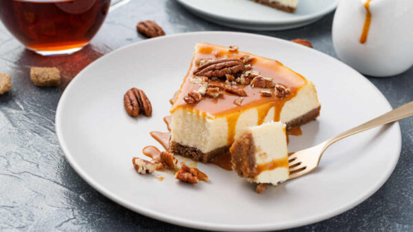 Pedaço de cheesecake clássico com calda de caramelo e nozes pecan.