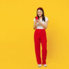 Comprimento do corpo em tamanho real de uma mulher jovem, sorridente, usando roupas casuais, usando um celular, isolada em fundo amarelo liso, em um retrato de estúdio.