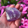 Um close-up de uma imagem de uma mão segurando um grande cristal de ametista roxo.