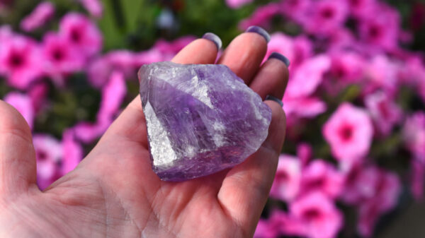 Um close-up de uma imagem de uma mão segurando um grande cristal de ametista roxo.
