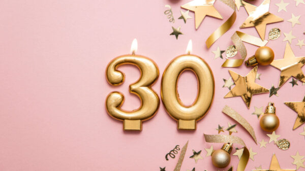 Velas de celebração douradas em formatos de número 3 e 0, e enfeites, em um fundo rosa.