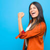 Jovem sentindo-se feliz, satisfeita e poderosa, flexionando o braço e mostrando o bíceps, contra uma parede plana.
