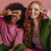 casal formado por uma mulher negra e uma mulher ruiva em fundo rosa
