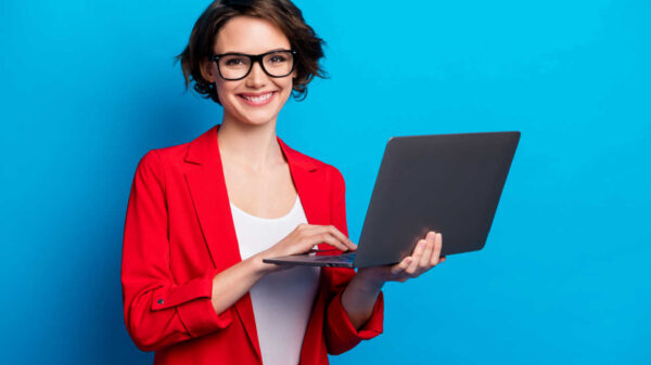 Retrato de mulher alegre, segurando na mão um laptop, isolada em um fundo de cor azul.