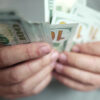 par de mãos segurando um leque de notas de dollar