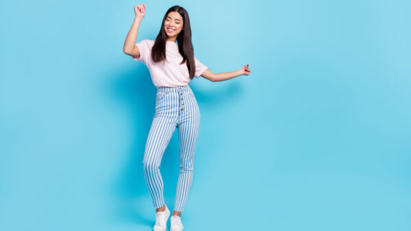 Foto de corpo inteiro de uma garota alegre e despreocupada, dançando e se movimentando, isolada sobre um fundo de cor azul.