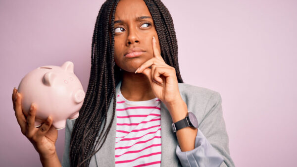 Mulher jovem economizando dinheiro em um cofrinho, sobre um fundo isolado, com um rosto sério, pensando em alguma questão, tendo uma ideia muito confusa.