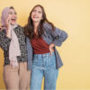 Duas mulheres rindo e se divertindo enquanto se abraçam. Uma delas está com uma mão no ombro da outra.