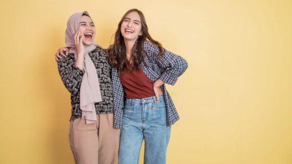 Duas mulheres rindo e se divertindo enquanto se abraçam. Uma delas está com uma mão no ombro da outra.