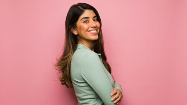 mulher de lado sorrindo e usando roupa verde. o fundo é rosa