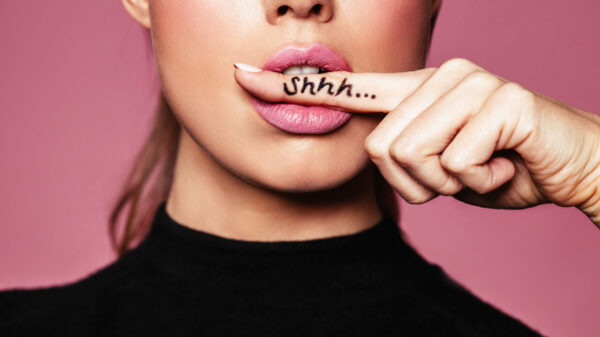 Conceito de segredos. Foto de uma mulher com um dedo na boca. Retrato de closeup da uma mulher fazendo um sinal de silêncio, com "shhh..." escrito no dedo.