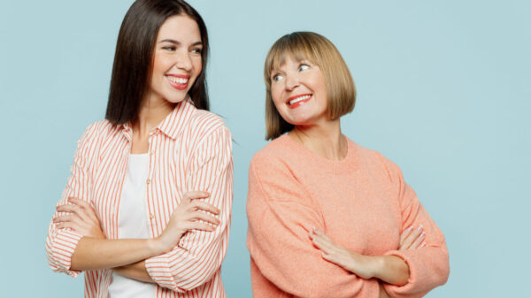 Mulheres sorrindo, juntas, vestindo roupas casuais, de braços cruzados, olhando uma para a outra, isoladas em um fundo azul ciano.