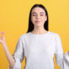 mulher fazendo o sinal zen de meditação com as mãos em fundo amarelo