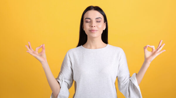 mulher fazendo o sinal zen de meditação com as mãos em fundo amarelo