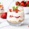 Sobremesa de tiramisu de morango com mascarpone, chantilly, migalhas de savoiardi e morango fresco, em um vidro, em cima de um mármore.