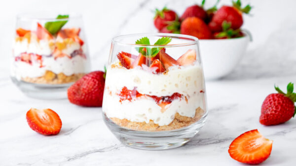 Sobremesa de tiramisu de morango com mascarpone, chantilly, migalhas de savoiardi e morango fresco, em um vidro, em cima de um mármore.