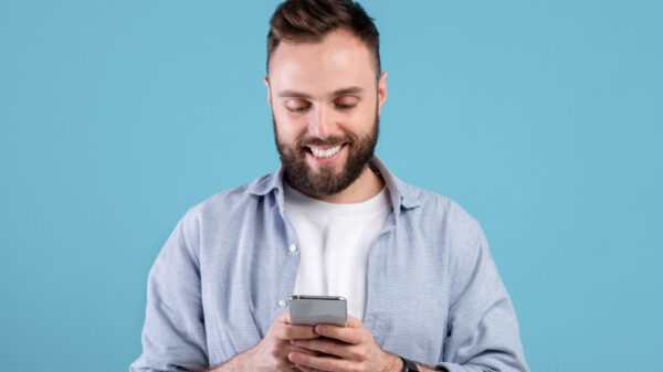 Conceito de vida online. Homem barbudo usando um celular, em um fundo azul de um estúdio. Homem jovem, positivo, com celular moderno, navegando na internet, postando nas mídias sociais.