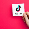 uma mão segurando um cartão com a logo do aplicativo tik tok em fundo pink