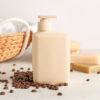 ao centro está um pote de shampoo e ao lado direito há grãos de café à direita está barras de sabonete e ao lado um cesto. o fundo é branco