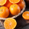 cesto com laranjas. fora do cesto, em uma mesa de madeira, há uma laranja cortada ao meio