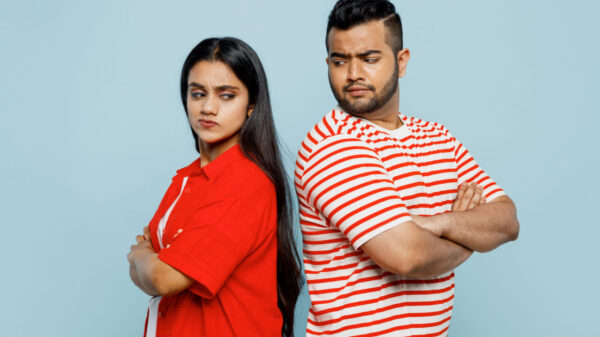 Casal ofendido um com o outro, usando roupas casuais vermelhas, um de costas para o outro, de braços cruzados, isolados em um fundo de cor azul pastel.