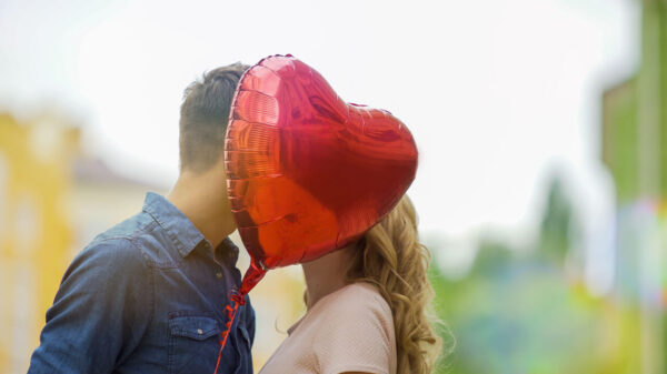 casal ao ar livre se beijando com um balão em formato de coração cobrindo os rostos