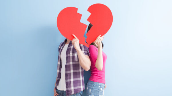 casal com um coração quebrado de papel cobrindo o rosto em fundo azul