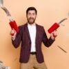 Foto de um homem muito feliz, com arminhas disparando notas de dinheiro, isolado em um fundo de cor bege.