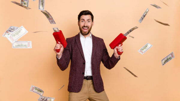 Foto de um homem muito feliz, com arminhas disparando notas de dinheiro, isolado em um fundo de cor bege.